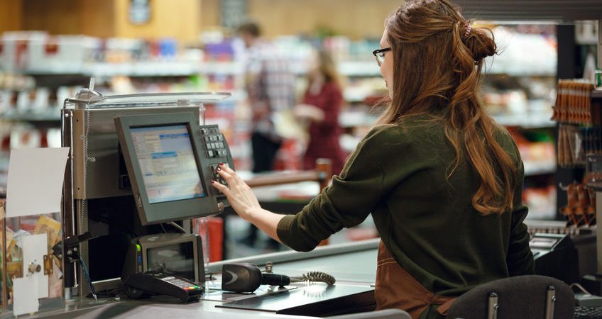 Back view photo of cashier woman on workspace in supermarket shop. Looking aside.